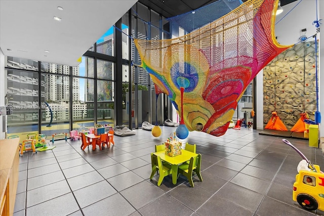 recreation room featuring expansive windows, a high ceiling, and a view of city