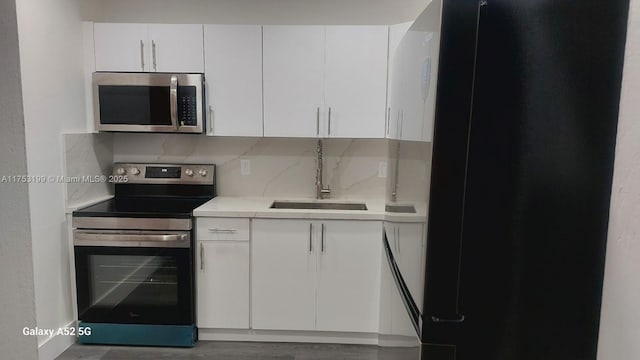 kitchen featuring tasteful backsplash, white cabinets, stainless steel appliances, light countertops, and a sink