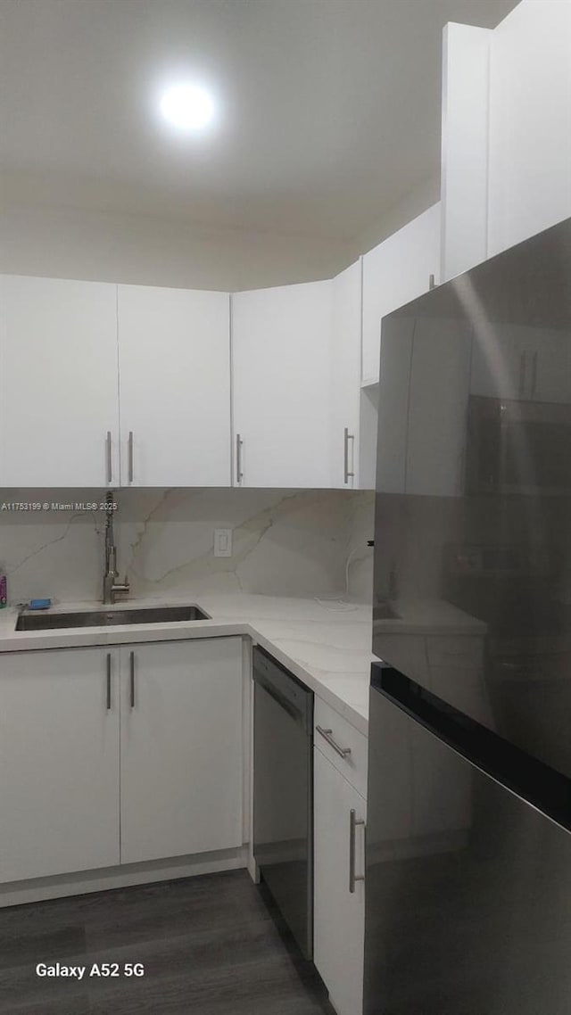 kitchen with dark wood finished floors, dishwasher, freestanding refrigerator, white cabinetry, and a sink