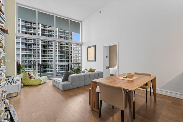 dining area featuring baseboards, wood finished floors, a towering ceiling, and floor to ceiling windows