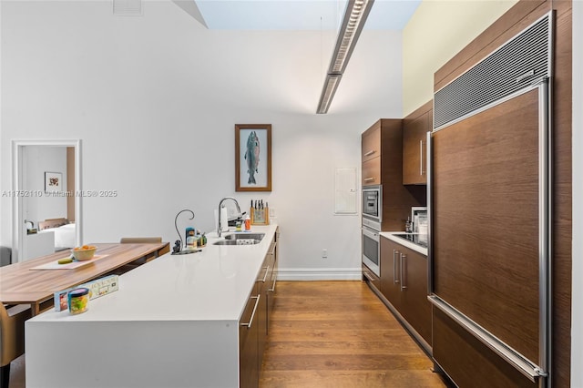 kitchen featuring built in appliances, dark wood-style flooring, a sink, light countertops, and modern cabinets