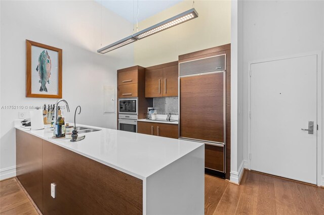 475 Brickell Ave Unit 2809, Miami, FL 33131 - kitchen with built in appliances, a sink, light wood-type flooring, a peninsula, and light countertops