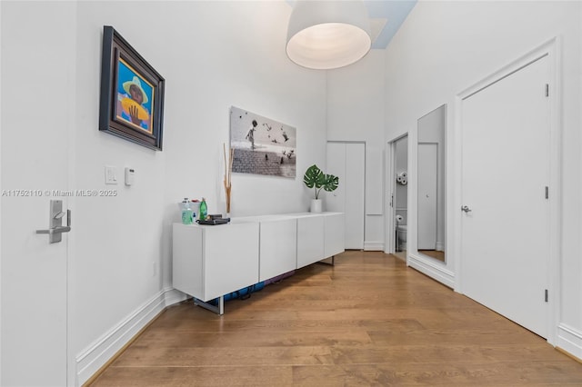 corridor with a towering ceiling, light wood finished floors, and baseboards