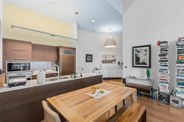 kitchen featuring tasteful backsplash, wood finished floors, a high ceiling, black microwave, and a sink