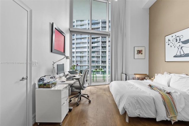 bedroom with access to exterior, expansive windows, and wood finished floors