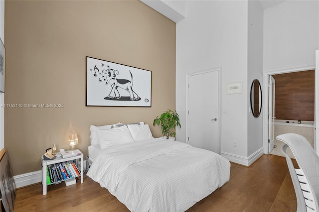 bedroom featuring a high ceiling, baseboards, and wood finished floors