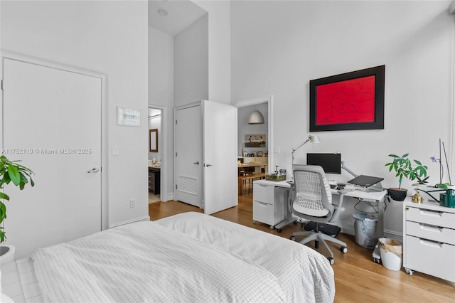 bedroom with a towering ceiling, ensuite bathroom, and wood finished floors