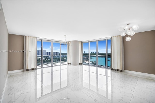 spare room featuring a notable chandelier, marble finish floor, a wall of windows, and baseboards