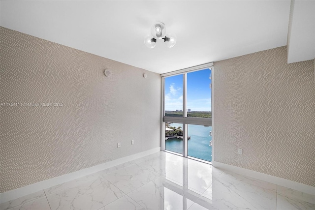 spare room with baseboards, marble finish floor, a wall of windows, and wallpapered walls