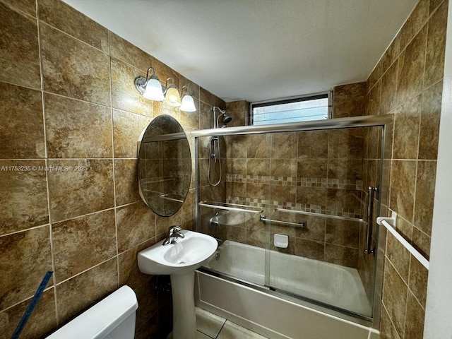 bathroom with bath / shower combo with glass door, toilet, and tile walls