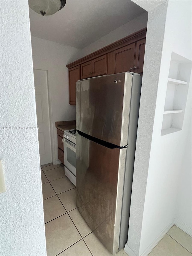 kitchen with built in shelves, light tile patterned flooring, white gas range oven, and freestanding refrigerator