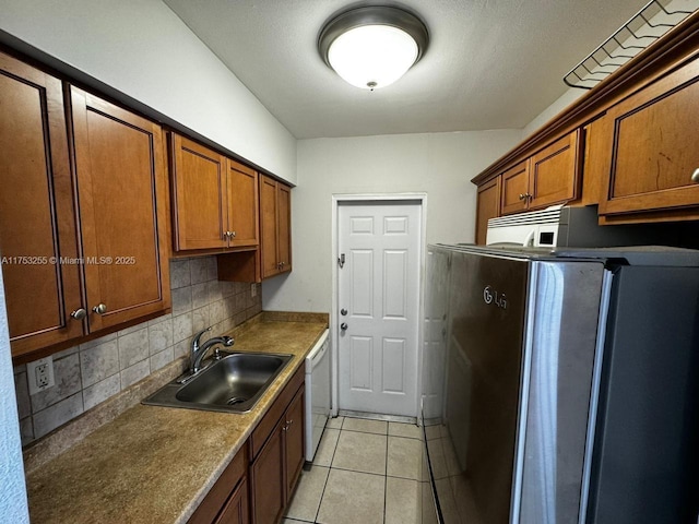 kitchen with light tile patterned floors, white appliances, a sink, tasteful backsplash, and brown cabinetry