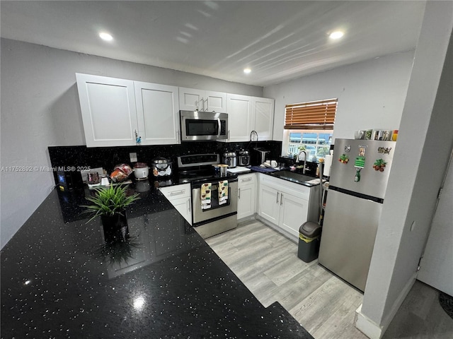 kitchen with a sink, white cabinets, appliances with stainless steel finishes, light wood-type flooring, and tasteful backsplash