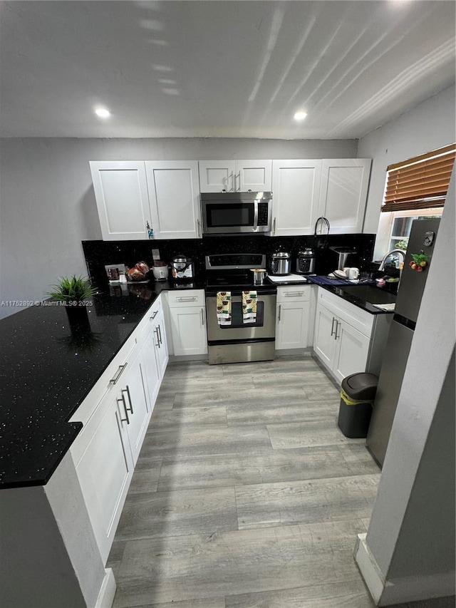 kitchen featuring stainless steel appliances, light wood finished floors, backsplash, and white cabinets