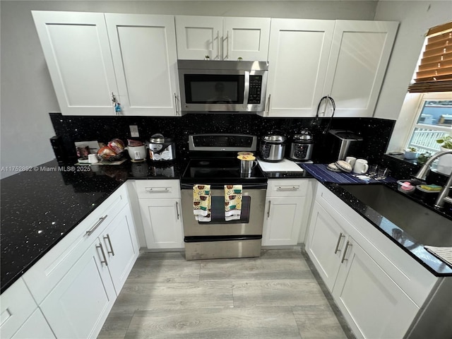 kitchen featuring appliances with stainless steel finishes, white cabinets, a sink, and decorative backsplash