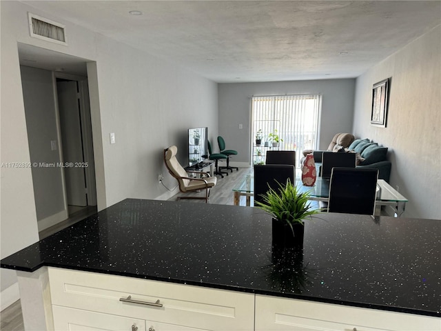 kitchen featuring white cabinetry, visible vents, open floor plan, and dark stone counters