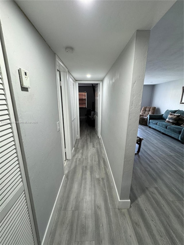 hallway with baseboards, wood finished floors, and a textured wall