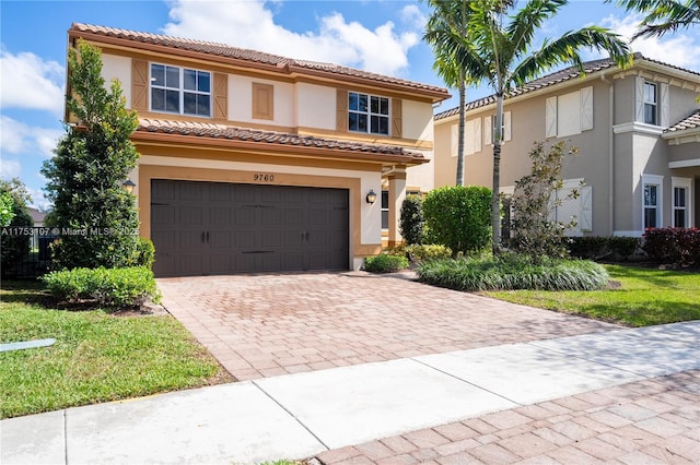 mediterranean / spanish house featuring an attached garage, a tiled roof, decorative driveway, and stucco siding