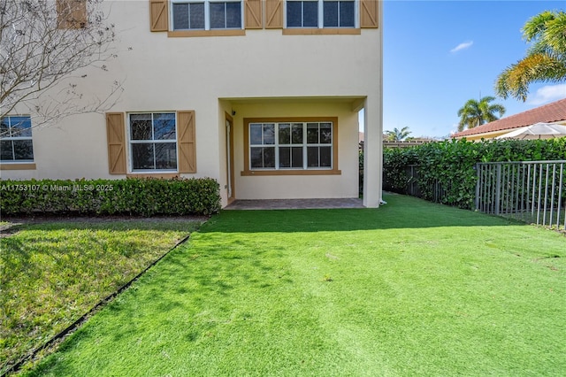 rear view of house featuring a yard, fence, and stucco siding