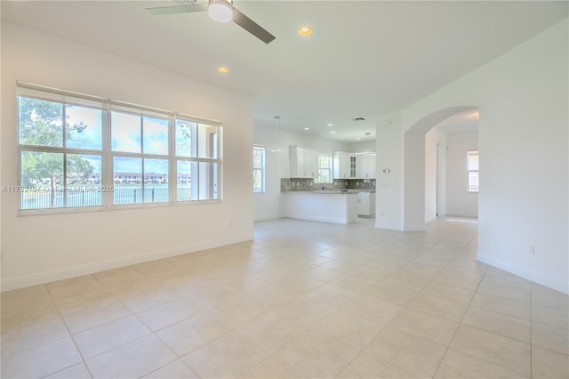 unfurnished living room featuring arched walkways, ceiling fan, light tile patterned floors, recessed lighting, and baseboards