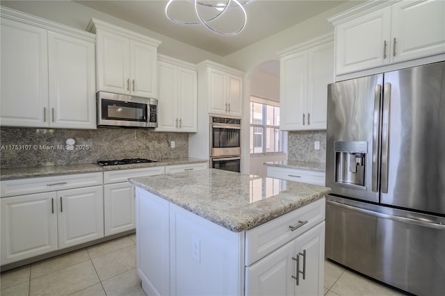 kitchen featuring arched walkways, light tile patterned floors, stainless steel appliances, white cabinetry, and a kitchen island