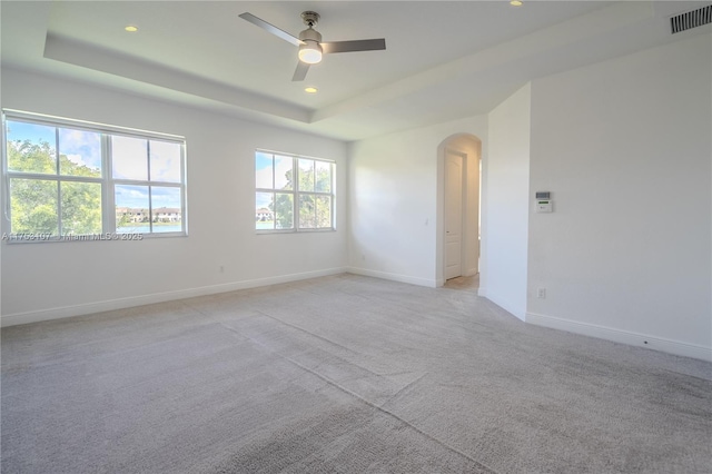 unfurnished room featuring arched walkways, light carpet, visible vents, baseboards, and a raised ceiling