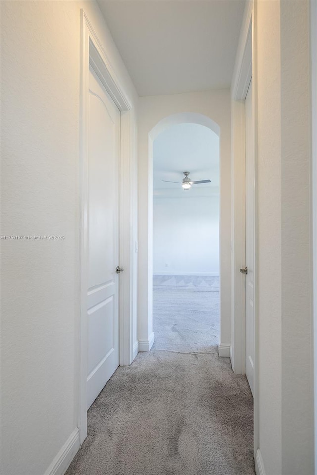 corridor featuring arched walkways, carpet, and baseboards