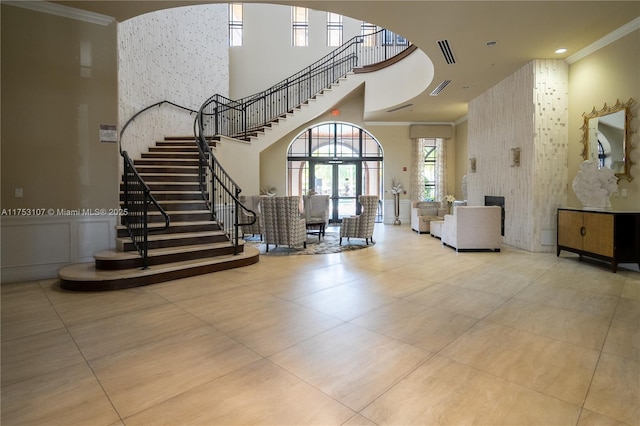 foyer entrance with crown molding, visible vents, a decorative wall, a towering ceiling, and stairs