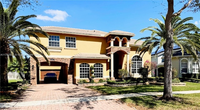 mediterranean / spanish house featuring a garage, stone siding, decorative driveway, and stucco siding