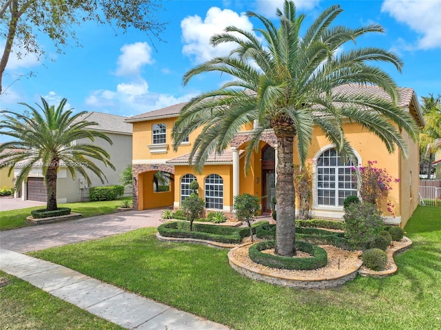 mediterranean / spanish home featuring a tiled roof, a front lawn, decorative driveway, and stucco siding