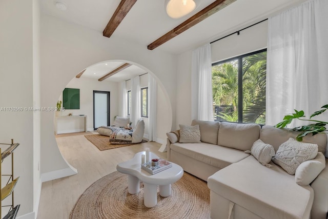 living room with arched walkways, wood finished floors, beam ceiling, and baseboards