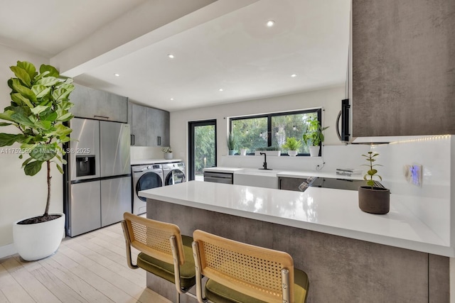 kitchen featuring a peninsula, separate washer and dryer, a sink, light countertops, and appliances with stainless steel finishes