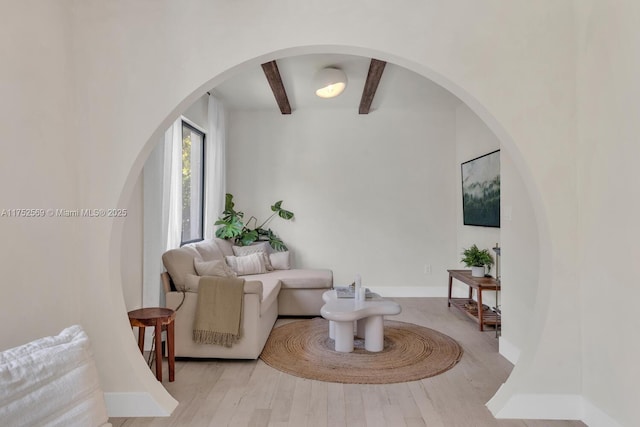 living area with light wood-style floors, beamed ceiling, and baseboards