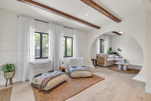 sitting room with arched walkways, beam ceiling, baseboards, and light wood finished floors