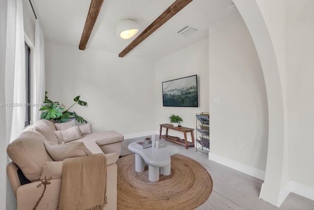 living room featuring beam ceiling, visible vents, light wood-style flooring, and baseboards