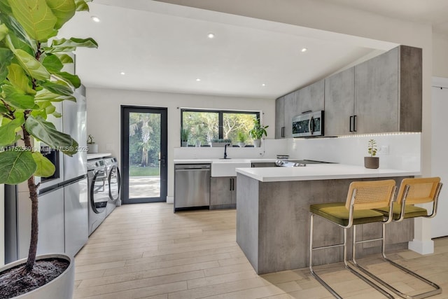 kitchen featuring washing machine and clothes dryer, stainless steel appliances, light countertops, light wood-type flooring, and a peninsula