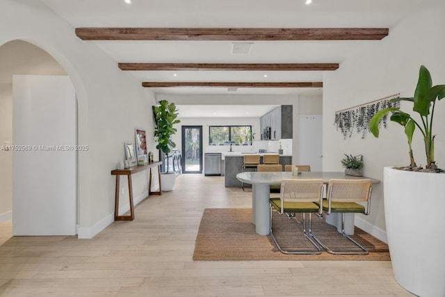 dining room featuring baseboards, visible vents, arched walkways, beamed ceiling, and light wood-type flooring