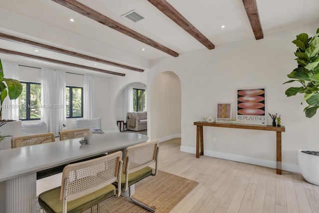 interior space featuring light wood-style flooring, arched walkways, baseboards, and beamed ceiling