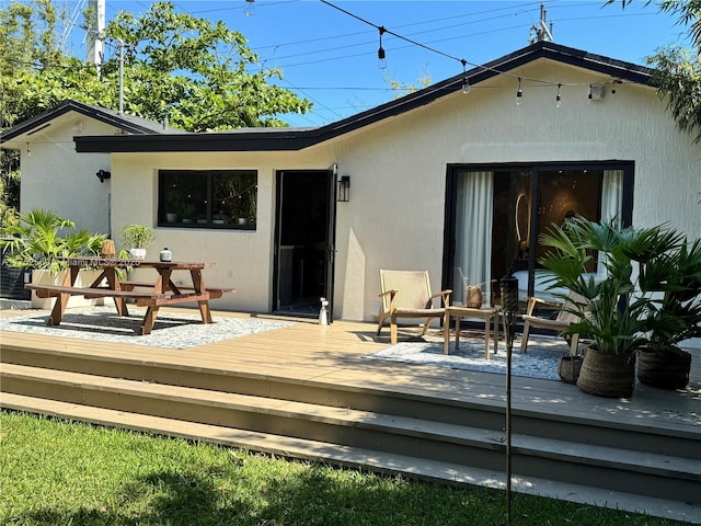 rear view of property featuring stucco siding and a wooden deck