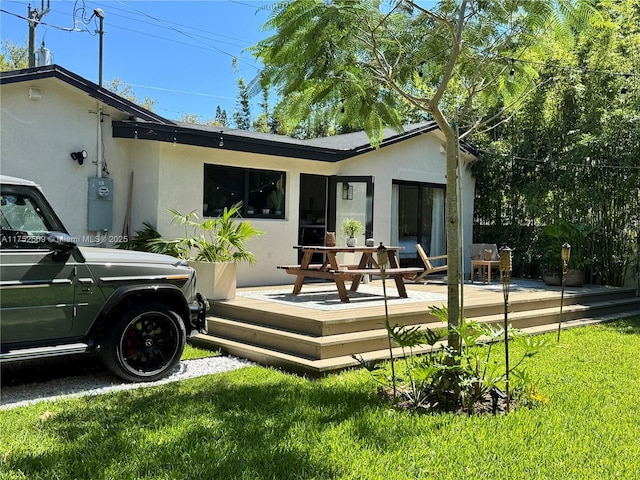 back of house featuring a yard, a wooden deck, and stucco siding