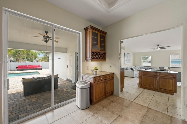 kitchen featuring ceiling fan, glass insert cabinets, brown cabinets, open floor plan, and light stone countertops