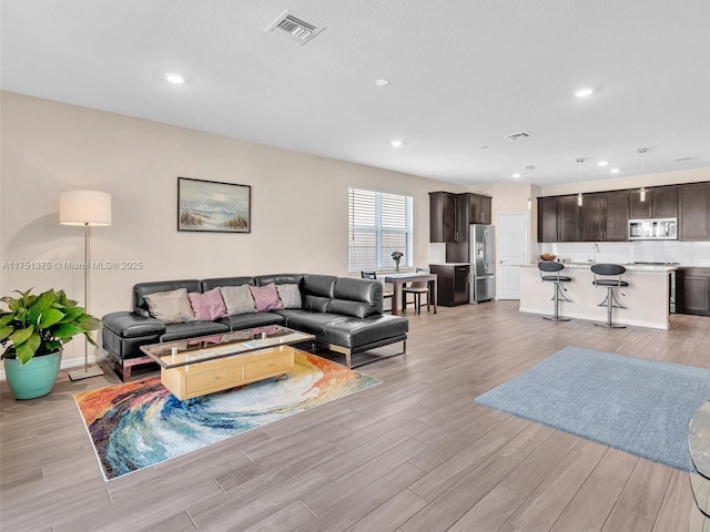 living room with light wood finished floors, visible vents, and recessed lighting