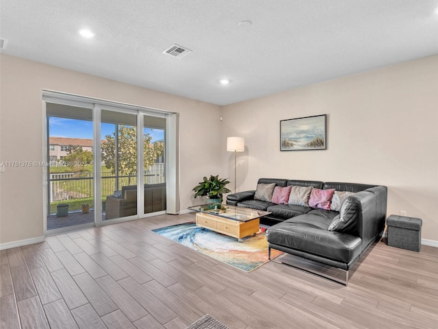 living room featuring a textured ceiling, wood finish floors, visible vents, and baseboards