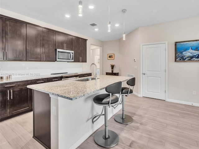 kitchen featuring light stone counters, visible vents, appliances with stainless steel finishes, a sink, and a kitchen breakfast bar