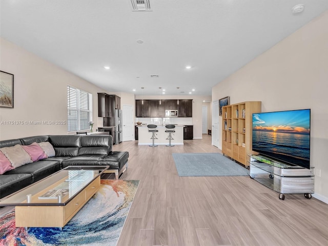 living room featuring baseboards, light wood-type flooring, visible vents, and recessed lighting