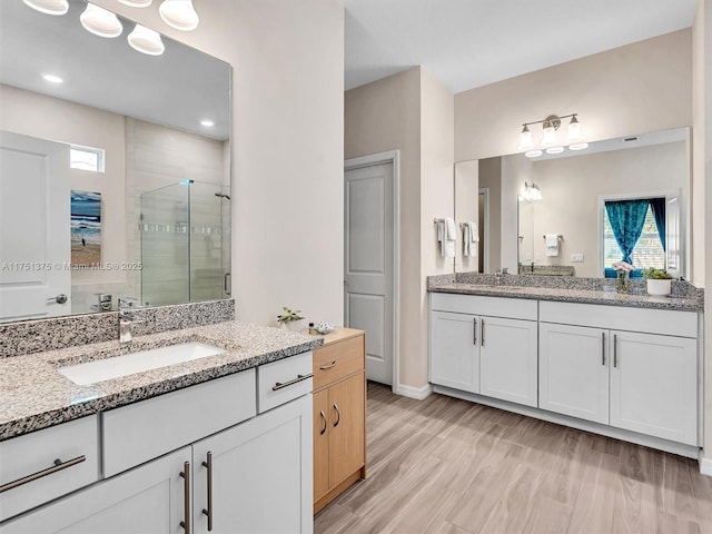 full bath featuring wood finished floors, two vanities, a sink, and a shower stall