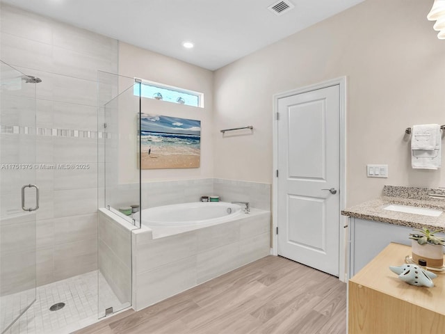 bathroom with a stall shower, visible vents, wood finished floors, vanity, and a bath