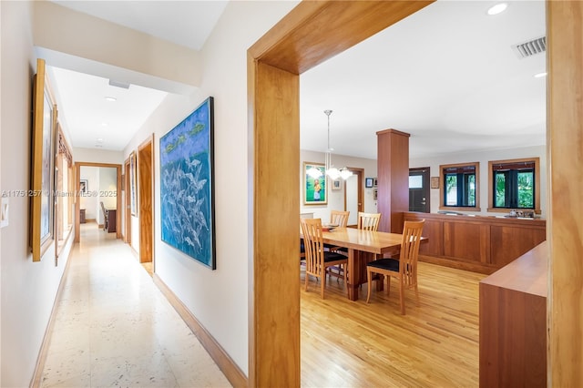 corridor with an inviting chandelier, light wood-type flooring, visible vents, and baseboards