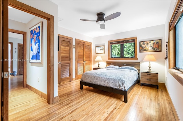 bedroom featuring baseboards, light wood finished floors, a ceiling fan, and multiple closets