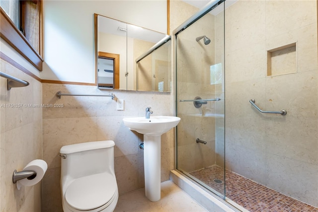 bathroom featuring tile patterned flooring, a shower stall, toilet, and tile walls